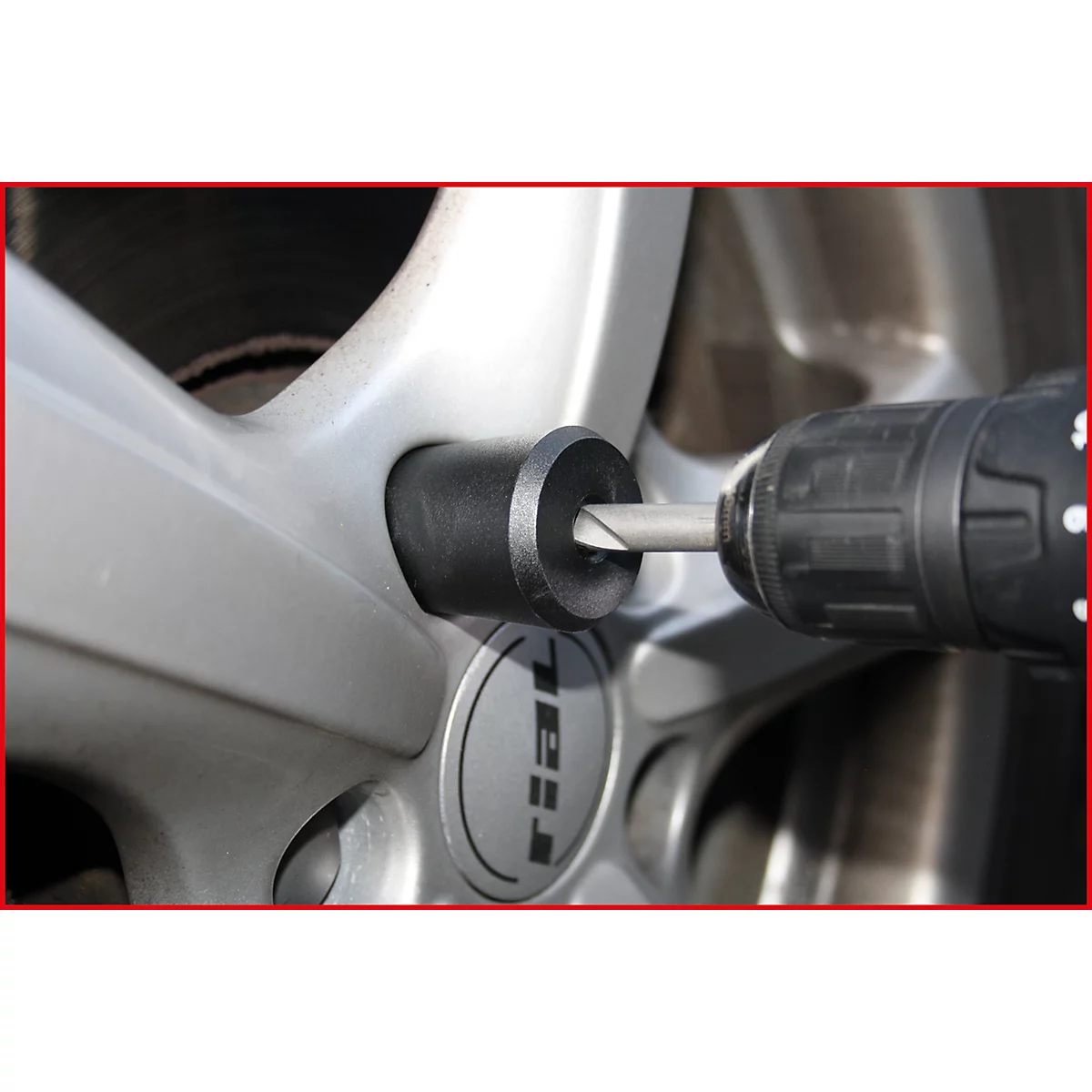 Ein Bohrer entfernt eine Radmutter von einer silbernen Felge. Das Wort "Rial" ist auf der Felge zu sehen.